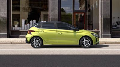 Hyundai i20 in lucid lime parked on the street in front of modern buildings.