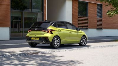 A green Hyundai i20 seen from the rear parked on a street.	