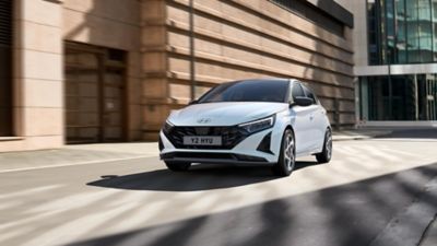 The Hyundai i20 driving in front of a modern building.