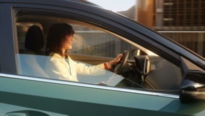 A woman sitting behind the wheel of her Hyundai Bayon, smiling and driving.