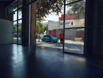 Imagen de un i10 aparcado junto a un viandante visto desde el interior de un edificio con amplias cristaleras.