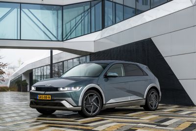 Driekwart vooraanzicht Hyundai IONIQ 5 geparkeerd voor een modern gebouw met veel glas.