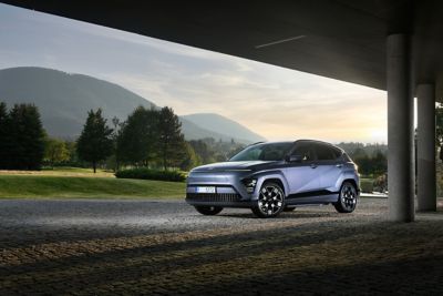 Driekwart vooraanzicht Hyundai KONA Electric, geparkeerd onder een brug met bergen op de achtergrond.