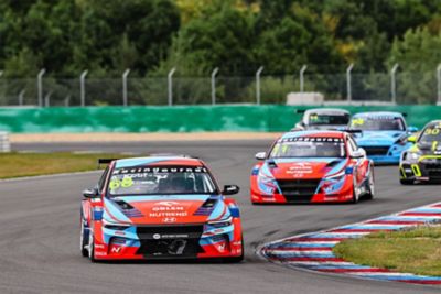 Závodní vozy Hyundai Elantra N TCR projíždějí zatáčkou na okruhu.