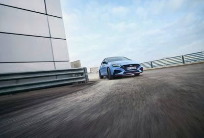 Ein Hyundai i30 N in Performance Blue fährt auf einer Teststrecke in eine Rechtskurve.