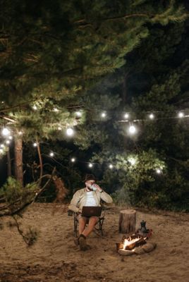 Man sat in camping chair whilst having a drink and working on his laptop. © Pavel Danilyuk