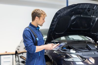 Modern bir otomobilin önünde Bluelink Mağazası uygulaması açık bir akıllı telefonu tutan kişi.