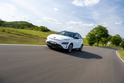 KONA Electric v bílé barvě jedoucí po okresní cestě ve slunečném počasí.