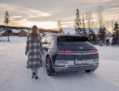 Woman walking towards the Hyundai IONIQ 5 in a winter landscape.