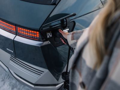 A woman plugging her Hyundai IONIQ 5 electric vehicle to a charging station.