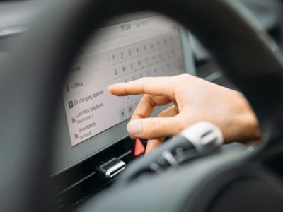 Eine Hand tippt auf ein Touchscreen-Display mit Ladestationsinformationen.