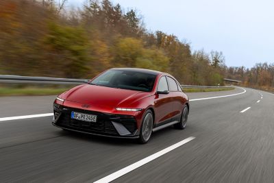 Driekwart vooraanzicht Hyundai IONIQ 6 op een weg door een bosrijke omgeving.