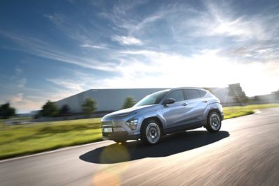 Driekwart vooraanzicht Hyundai KONA Electric rijdend op een weg met berg op de achtergrond.