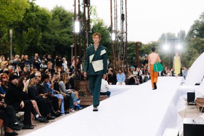 Twee modellen, een vrouw en een man, lopend op een catwalk met zittend publiek ernaast.