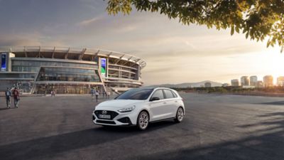 Ein weißer Hyundai i30 N Line, schräg von vorne, steht vor einem Stadion.