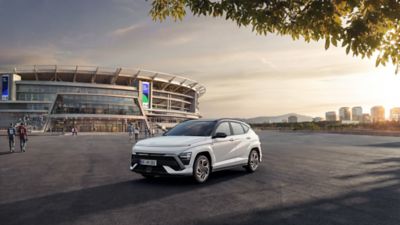Ein weißer Hyundai KONA N Line, schräg von vorne, steht vor einem Stadion.