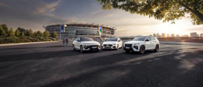 Drei Hyundai N Line Modelle in weißer Außenfrabe stehen im Halbkreis geparkt vor einem Stadion