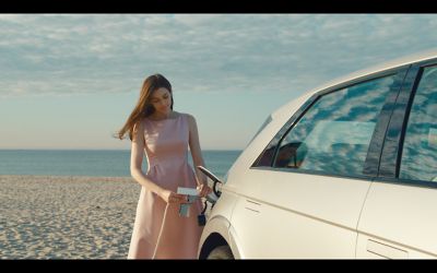 Ragazza con vestito elegante ricarica IONIQ 5 sulla spiaggia.