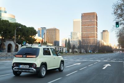 Driekwart achteraanzicht Hyundai INSTER, rijdend in de stad richting een verkeerslicht.