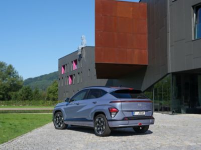 Driekwart achteraanzicht Hyundai KONA Electric geparkeerd voor modern gebouw.