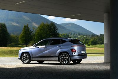 Zijaanzicht Hyundai KONA Electric geparkeerd onder een brug met berglandschap op de achtergrond.
