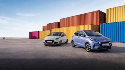 Two i10 parked in front of colourful containers.