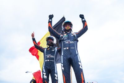 Die Hyundai Rally-Fahrer Thierry Neuville und Martijn Wydaeghe beim Siegerjubel vor einer belgischen Flagge.