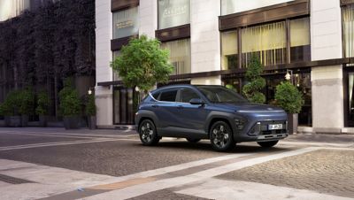 Ein blauer Hyundai KONA parkt vor einem innerstädtischen Gebäude.