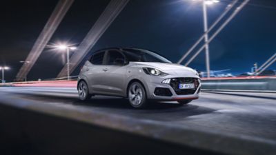 Ein weißer Hyundai i10 N Line, fährt, von links kommend, bei Nacht über eine Brücke.