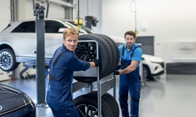 Zwei Hyundai Service-Techniker schieben einen Rollwagen mit Reifen durch eine Werkstatt.