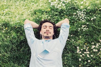 Ein Mann mit Kopfhörern und Smartphone liegt mit hinter dem Kopf verschränkten Armen im Gras.