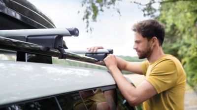 Ein Mann in einem gelben T-Shirt montiert den Dachträger auf einem Hyundai Fahrzeug.