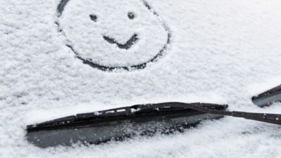 Eine schneebedeckte Autoscheibe, auf die ein Smiley gemalt wurde.