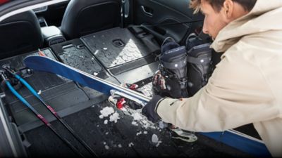 Skier und Skischuhe mit Schneeresten werden in ein Hyundai Fahrzeug gepackt, das mit einer Kofferraum-Formschalenmatte ausgestattet ist.
