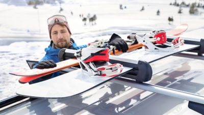 Ein Mann im Winteroutfit befestigt Skier und Snowboard am Hyundai Ski- und Snowboardträger.
