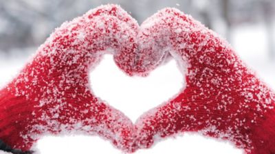 Hände in schneebedeckten roten Handschuhen formen ein Herz.