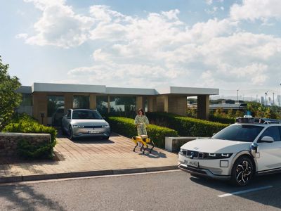En kvinna och en Spot-robot närmar sig en IONIQ 5-robotaxi utanför ett hus.