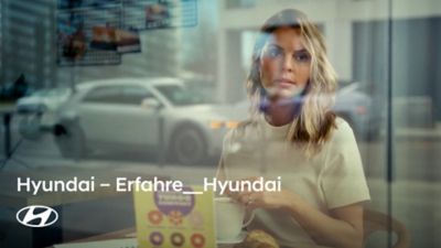 Eine Frau schaut durch ein Fenster. Im Hintergrund sieht man einen Hyundai IONIQ 5.