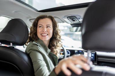 Eine Frau sitzt am Steuer und dreht sich nach hinten um. 