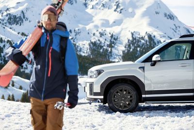 Ein Mann mit Skiausrüstunge entfernt sich von einem Hyundai SANTA FE, der in einer Schneelandschaft geparkt ist.