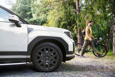 Ein Mann mit Fahrrade entfernt sich von einem Hyundai SANTA FE, der auf einem Waldweg geparkt ist.