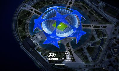 Flygvy över en upplyst fotbollsarena formad som UEFA Champions League-logotypen