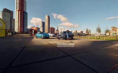 Eine Frau im blauen Kleid lehnt an einen Hyundai TUCSON. Dahinter zwei weitere Hyundai Modelle vor einer Hochhauskulisse.
