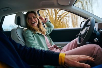 Frau auf dem Fahrersitz eines parkenden Hyundai IONIQ 5 dreht sich lächelnd zu ihrem Beifahrer hin.