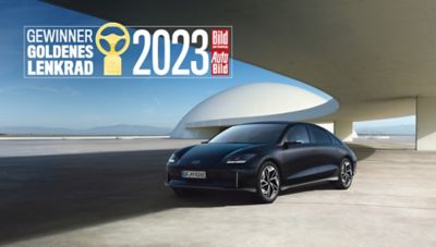 Der Hyundai IONIQ 6 vor einem futuristischen Gebäude mit dem Logo Goldenes Lenkrads 2023.