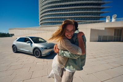 Eine lachende Frau umarmt einen Mann vor einem Hyundai IONIQ 5.