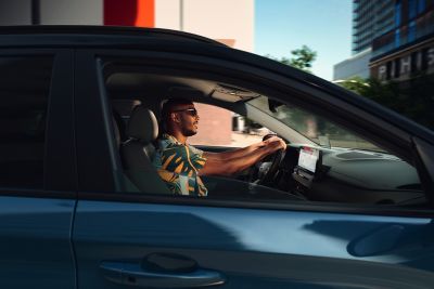 Ein Mann mit Sonnenbrille, lächelnd, am Steuer seines Hyundai.