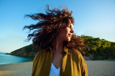 Eine Frau am Strand lässt ihre Haare im Wind tanzen.