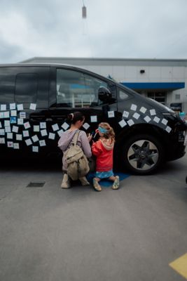 Mutter und Kind beim Bekleben und Bemalen eines Hyundai STARIA.