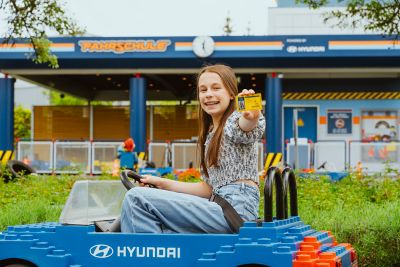 Ein lachendes Mädchen sitzt in einem Fahrzeug der Legoland Fahrschule powered by Hyundai und zeigt ihren Führerschein